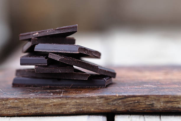 Stack of broken chocolate bar pieces Stack of broken dark chocolate bar pieces on a wooden background. Horizontal dark chocolate stock pictures, royalty-free photos & images