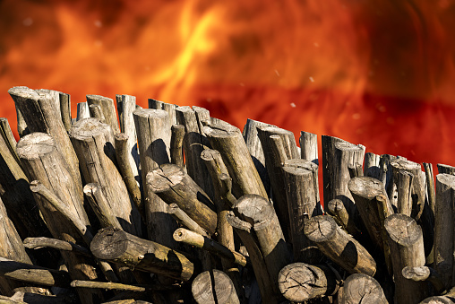 Closeup of a stack of firewood with blurred flames of a bonfire on background with copy space.