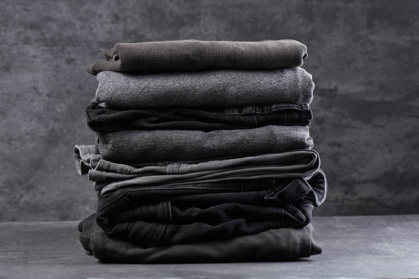 A stack of neatly folded dark clothes isolated on a black gray background close-up stock photo
