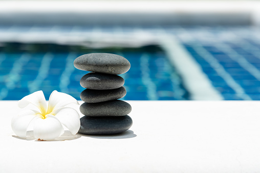 Stack of pebble stones with plumeria flower near swimming pool