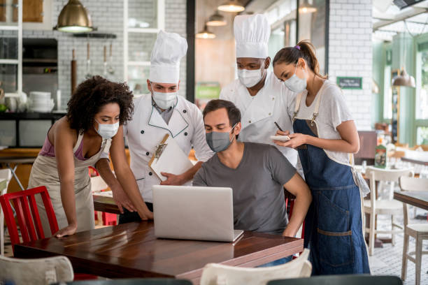 Staff meeting at a restaurant wearing facemasks Staff meeting with the business owner of a restaurant wearing facemasks and preparing for reopening during the COVID-19 pandemic restaurant employee management stock pictures, royalty-free photos & images