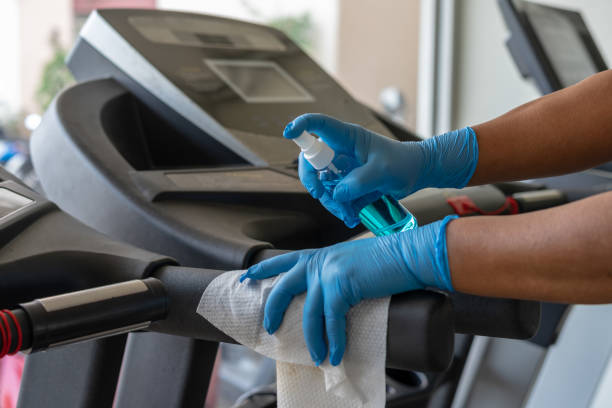 工作人員使用濕巾和藍色消毒劑從瓶子清潔跑步機在健身房。防腐劑,消毒,清潔和保健,抗冠病毒(covid-19)。 - 健身房 個照片及圖片檔