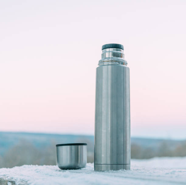 Stainless thermos and cup on snowy background. stock photo