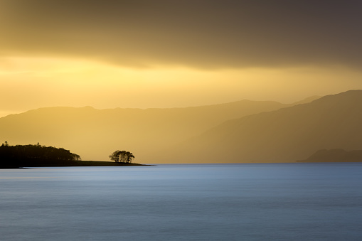 A view across Loch Linnhe in Scotland. A group of trees stand silhouetted against a dramatic yellow light