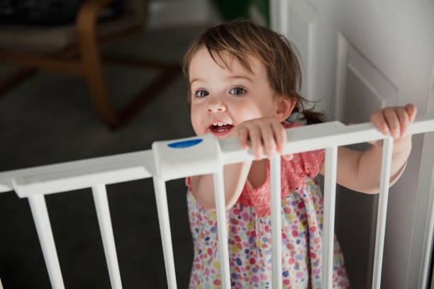 Standing at the Saftey Gate Front view of a little girl standing on the other side of a baby saftey gate. The little girl is holding onto the top of the saftey gate and looking at the camera over the top. gate stock pictures, royalty-free photos & images