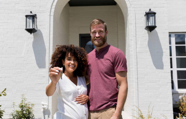 Standing by husband, pregnant wife holds keys to new house Standing by her husband at the front door, the pregnant woman holds the keys to their new house. in front of stock pictures, royalty-free photos & images