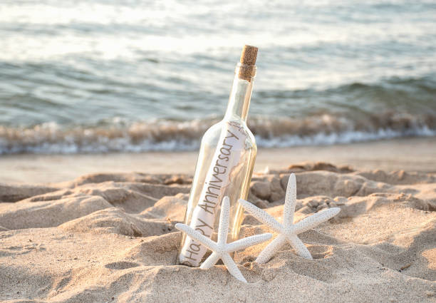 starfish with anniversary message in bottle pair of white starfish in beach sand with happy anniversary message in a bottle on the seashore wedding anniversary stock pictures, royalty-free photos & images