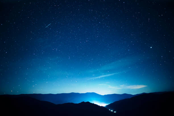 starry night sky over mountains panorama with city lights below - milky way imagens e fotografias de stock