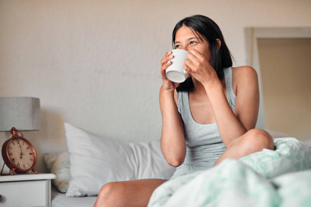 Start the day with coffee and serenity Shot of a young woman enjoying a relaxing cup of coffee in bed at home sunday morning coffee stock pictures, royalty-free photos & images
