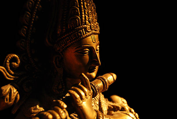 Statue of the Hindu God Krishna playing a flute Statue of Hindu God - Krishna in direct Sunlight. Background cleaned and made black. Very slight grains in dark areas. Depth of field - focus vertically through centre of forehead. vishnu stock pictures, royalty-free photos & images