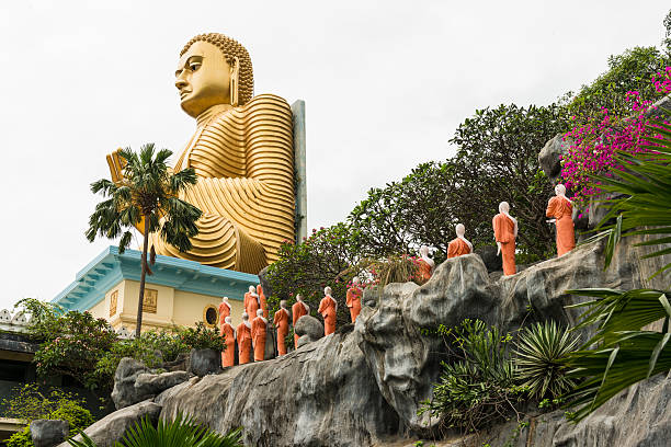 Statues of Buddha in Dambulla Golden Temple in Sri Lanka Statues of Buddha in line and large golden Buddha on top of rock at the Temple house in the caves known as Dambulla royal cave Temple or Golden Temple, which is one of UNESCO World Heritage sites in Sri Lanka. There are around 153 statues of Buddha representing everyday life, some statues of kings and Hindu gods. The ceiling has picturesque paintings as well. dambulla stock pictures, royalty-free photos & images