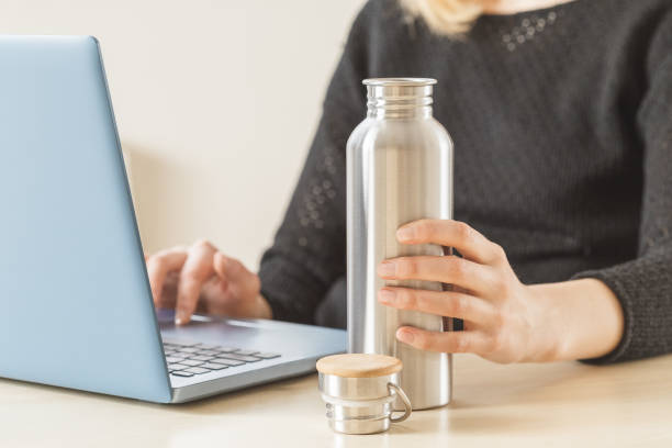 Stay hydrated during work from home or office White woman holding her personal stainless steel water bottle on the working table. Daily hydration habit to stay healthy reusable water bottle stock pictures, royalty-free photos & images