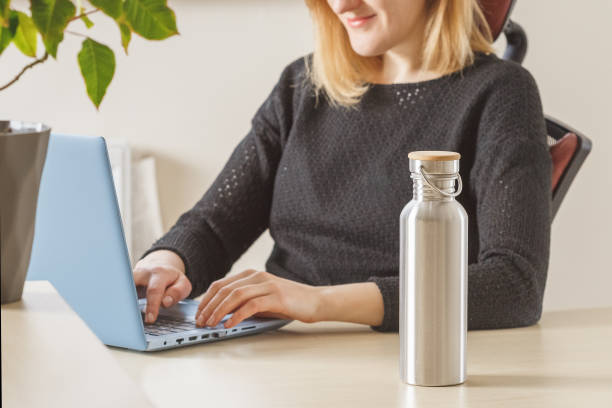 Stay hydrated during work from home or office Woman keeps her steel water bottle on the table to hydrate herself during working day at home or office. Focus on the bottle reusable water bottle stock pictures, royalty-free photos & images
