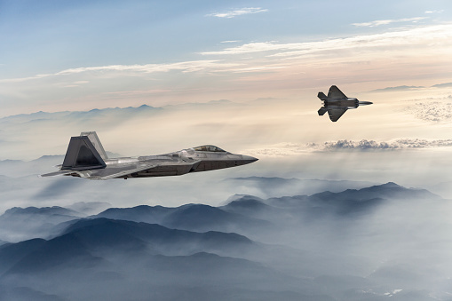 F-22 Stealth Jet Fighters flying over fogy mountains at sunset