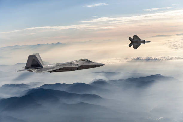 F-22 Stealth Jet Fighters flying over fogy mountains at sunset F-22 Stealth Jet Fighters flying over fogy mountains at sunset defense industry stock pictures, royalty-free photos & images
