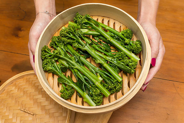 Steamed Broccoli Girl holding bamboo pan with steamed broccoli rabe. Broccoli is prepared and ready to eat. broccoli rabe stock pictures, royalty-free photos & images