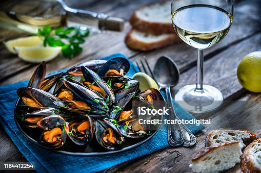 istock Steamed mussels and white wine on rustic wooden table 1184412254