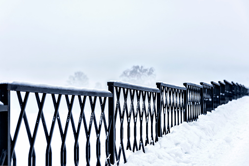 Steel fence along the embankment of the river during the fog in winter in severe frost