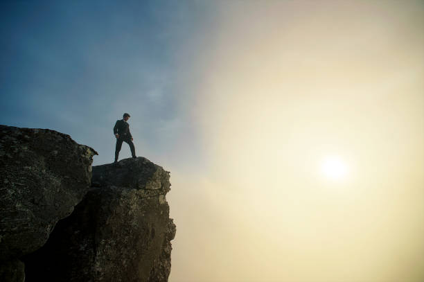 Stepping out Side Angle low angle view of a businessman at sunset on top of a cliff with dramatic sky and clouds below and above Cape Town South Africa cliff stock pictures, royalty-free photos & images