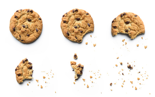 An overhead photo of chocolate chips cookies with a slice of chocolate, shot from above on a piece of baking paper, with copy space