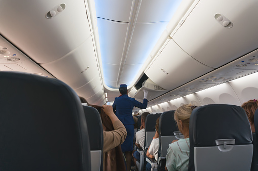 スチュワーデスは旅客機の機内の荷物棚を閉めます飛行の快適性と安全性を確保します ギリシャのストックフォトや画像を多数ご用意 Istock