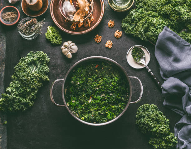 Stewed kale in cooking pot on rustic kitchen table with ingredients for vegan kale recipes: nuts,garlic, olives oil, top view. stock photo