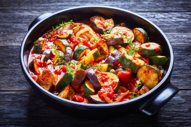 Stewed vegetables eggplant, tomatoes, zucchini with tomato sauce, garlic and herbs stock photo