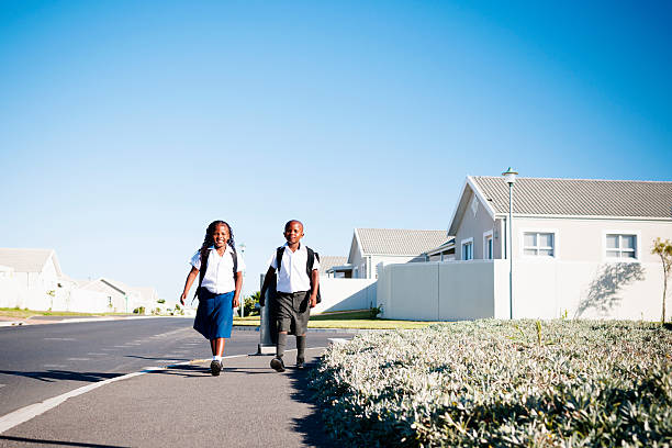 Stick To The Sidewalk Smiling young brother & sister in school uniform walking on the sidewalk to school school district stock pictures, royalty-free photos & images