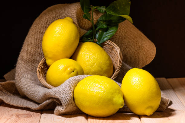 still life of lemons with green leaves on wood, burlap and wicker basket stock photo