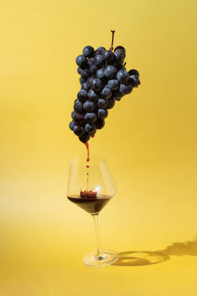 Still life with black grapes and flowing red wine into a glass on yellow background stock photo