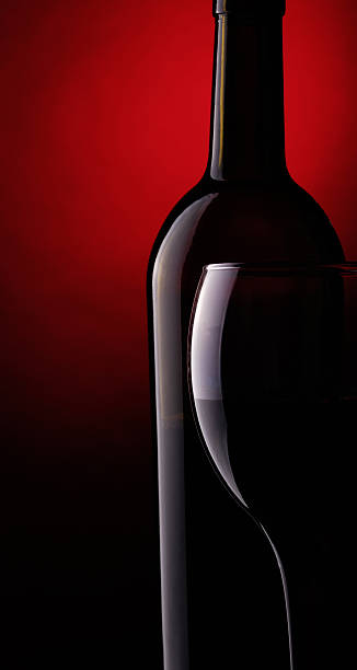 Still life with bottle and glass of red wine on a dark red background.