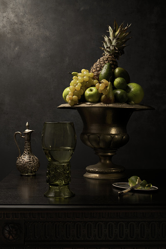 Art photography of antique table, with fruit bowl, silver carafe and silver fruit knife, big glass of white wine in old, german Roemer renaissance large glass goblet. Dutch masters oil painting style. Ready to print!