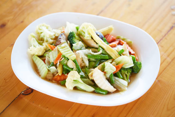 Stir Fried Mixed Vegetables (Sliced baby corn, oringi mushrooms, shiitake, carrots, kale, cauliflower, cauliflower and yard long beans) are served with white plate on wooden table. good healthy food stock photo