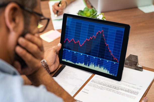 Stock market crash Closeup of a stock market broker working with graphs on digital tablet at office. Rear view of stock agent reading bad report and graph. Back view of multiethnic businessman analyzing fall sales. stock market  stock pictures, royalty-free photos & images