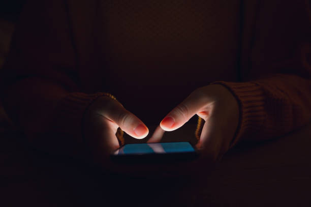 Stock photo of a woman's hands using smartphone in the dark stock photo