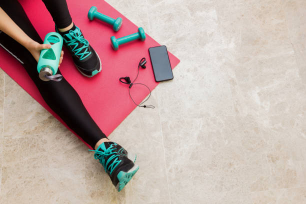 Stock photo of a young woman resting after exercising at home Stock photo of a young woman resting after exercising at home in the living room with a bottle and some objects exercising stock pictures, royalty-free photos & images