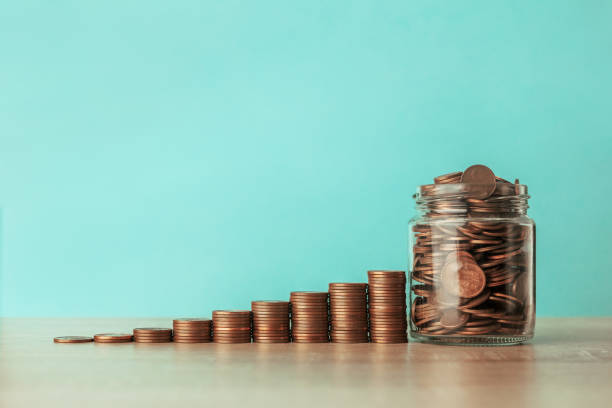 Stock photo of an ascending staircase of coins on a blue background with a jar full of coins. Saving concept stock photo