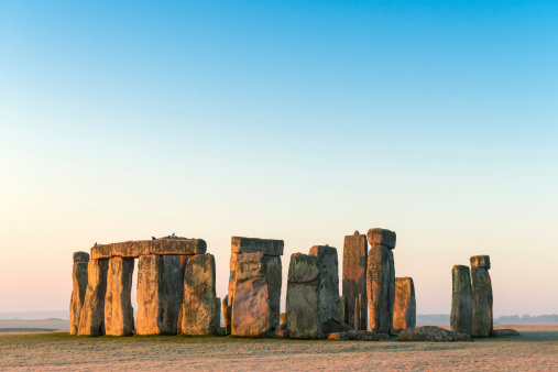 A wide angle view of Stonehenge in the landscape of Salisbury Plain, with the first light on a cold frosty morning.