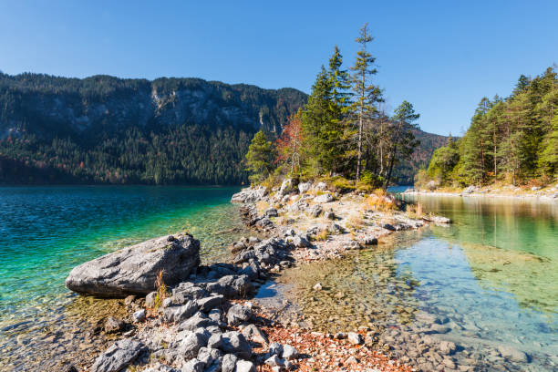 Stones on the shore of the headland over to island Braxeninsel in the Lake Eibsee surrounded by autumn forest, Bavaria, Germany stock photo