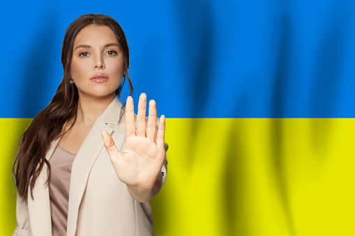 Stop gesture. Woman showing stop gesture on Ukrainian flag background. No war in Ukraine, save Ukraine concept