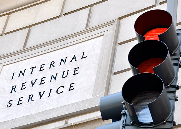 Stop, pay your taxes! Internal Revenue Service sign with a traffic signal in the foreground indicating a red light. irs stock pictures, royalty-free photos & images