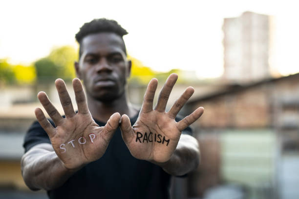 "Stop Racism" message concept African-American man standing outdoors and looking at the camera. He's showing a message that says "Stop Racism" on his hands. racism stock pictures, royalty-free photos & images