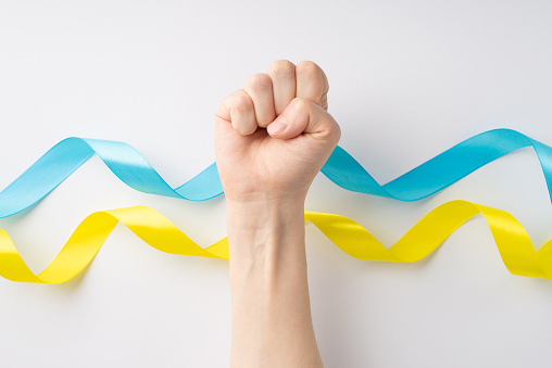 Stop the war in Ukraine concept. First person view photo of raised female hand with clenched fist over national flag on isolated white background