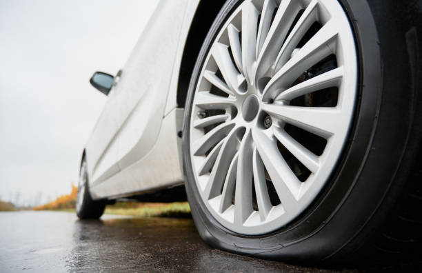Stopped white car with punctured car tire on a roadside stock photo