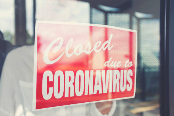 Store owner putting up a closed sign in the window Store owner putting up a closed sign in the window. Sign says: closed due to coronavirus closed stock pictures, royalty-free photos & images