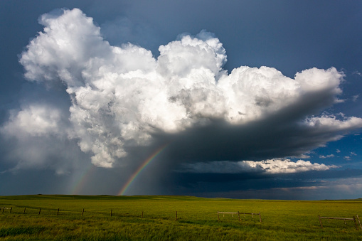 Storm cloud with silver lining and double rainbow over green field in Montana