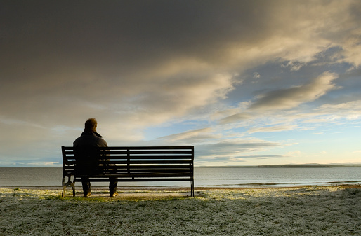 Man sitting on bench looking out at storm clouds approaching.