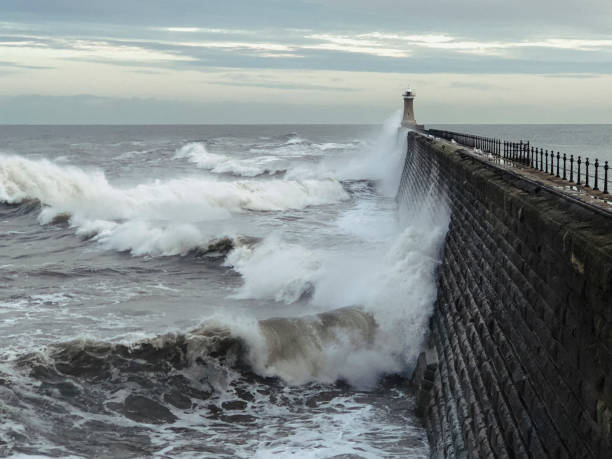 Stormy Day on the Coast Waves crashing against a brick pier during a stormy day in Summer. A lighthouse is just noticeable at the end of the pier north pier stock pictures, royalty-free photos & images