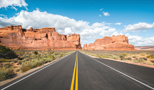 Straight highway road with yellow dividing lines seen in Arches National Park a beautiful sunny day.