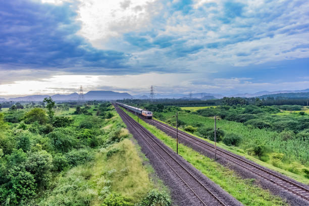 straight railway track goes to horizon in green landscape under blue sky with clouds. stock photo